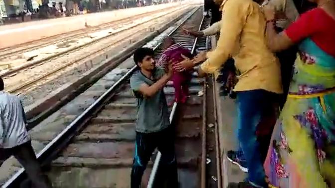 Gambar dari video pada 20 November 2018, seorang pria India menggendong bayi dan memberikan kepada ibunya  setelah terjatuh di samping rel di stasiun kereta api di Mathura, Uttar Pradesh. Bayi satu tahun itu selamat tanpa luka sedikitpun. (NNIS / AFP)