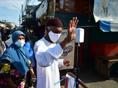 Seorang pria mengukur suhu tubuhnya sebelum memasuki pasar untuk membeli makanan, sebagai bagian dari upaya untuk menghentikan penyebaran virus corona Covid-19, selama bulan suci Ramadhan di provinsi selatan Thailand, Narathiwat (17/4/2021). (AFP/Madaree Tohlala)