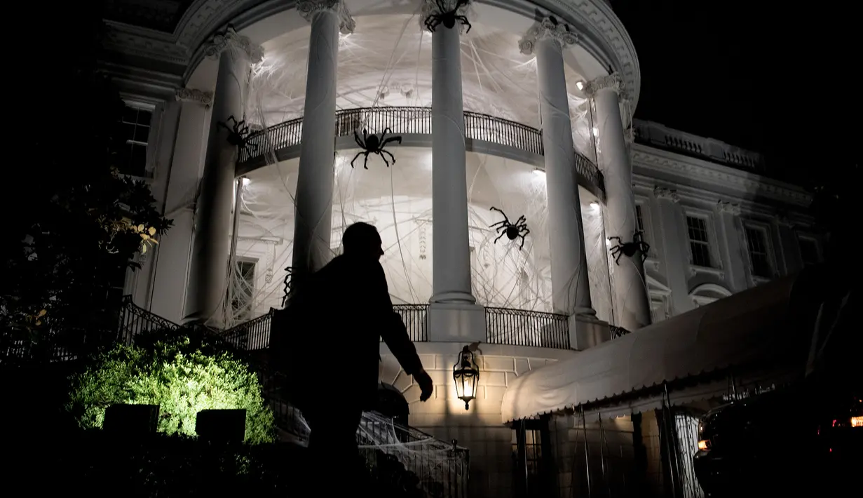 Petugas keamanan berjalan di depan pelataran Gedung Putih yang dipenuhi laba-laba raksasa di Washington DC, AS, Sabtu (28/10). Laba-laba raksasa tersebut merupakan boneka yang sengaja dipasang dalam rangka menyambut Halloween. (Brendan Smialowski / AFP)