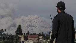 Seorang pria menyaksikan Gunung Sinabung memuntahkan abu saat erupsi terlihat dari Kabupaten Brastagi di Karo, Sumatera Utara (11/3/2021). Gunung berapi tersebut mengeluarkan longsoran awan gas membakar yang mengalir menuruni lerengnya saat terjadi letusan pada hari Kamis. (AFP/Sugeng Nuryono)