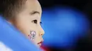Seorang anak memakai salah satu maskot Olimpiade di wajahnya saat menonton perlombaan speedskating 1.500 meter putri di Gangneung Oval pada Olimpiade Musim Dingin PyeongChang 2018 di Gangneung, Korea Selatan, 12 Februari 2018. (AP Photo/John Locher)