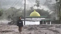 Seorang pria berjalan melewati masjid yang sebagian tertutup abu vulkanik dari letusan Gunung Semeru di desa Kajar Kuning di Lumajang, Jawa Timur, Indonesia, Senin, 5 Desember 2022. Gunung berapi tertinggi di Indonesia pada hari ini Senin (5/12/2022), masih mengeluarkan awan panas guguran dengan amplitudo 25 mm dan lama gempa 386 detik. (AP Photo/Imanuel Yoga)
