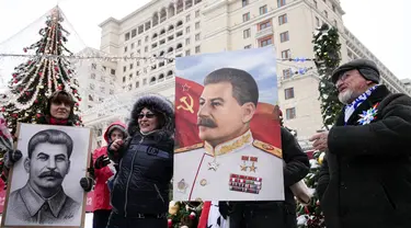 Orang-orang berfoto sambil memegang potret pemimpin Soviet Josef Stalin sebelum meletakkan bunga di makamnya menandai peringatan 142 tahun kelahirannya di dekat Tembok Kremlin di Lapangan Merah di Moskow, Rusia, Selasa (21/12/2021). (AP Photo/Alexander Zemlianichenko)