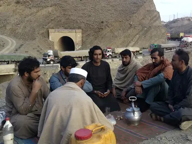 Pengemudi minum teh hijau di dekat truk mereka yang terdampar sarat dengan persediaan untuk Afghanistan, berbaris di jalan raya saat mereka menunggu untuk membuka titik penyeberangan Torkham, yang ditutup oleh penguasa Taliban Afghanistan, di Landi Kotal, daerah distrik Khyber Pakistan di sepanjang perbatasan Afghanistan, Selasa (21/2/2023). Penutupan pos lintas batas utama antara Pakistan dan Afghanistan yang sudah berlangsung tiga hari menyebabkan ribuan kendaraan pengangkut barang terjebak di perbatasan. (AP Photo/Qazi Rauf)