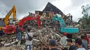 Sejumlah warga menyaksikan alat berat mencari korban di reruntuhan gedung pemerintah daerah yang runtuh saat gempa bumi di Mamuju, Sulawesi Barat, Jumat (15/1/2021). (AP Photo/Azhari Surahman)