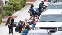 Para penumpang berlindung di samping kendaraan saat terjadi penembakan di Bandara Fort Lauderdale, Florida, AS (6/1). Ratusan orang dilaporkan berada di sekitar lokasi saat penembakan terjadi. (AP Photo/Wilfredo Lee)