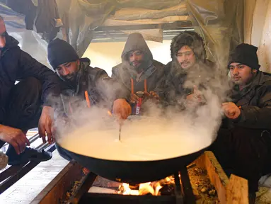 Para imigran memasak dalam tempat penampungan sementara di Kamp Lipa, luar Bihac, Bosnia, Jumat (8/1/2021). Cuaca bersalju dan musim dingin telah membawa lebih banyak penderitaan bagi ratusan imigran yang terjebak selama berhari-hari di kamp tersebut. (AP Photo/Kemal Softic)