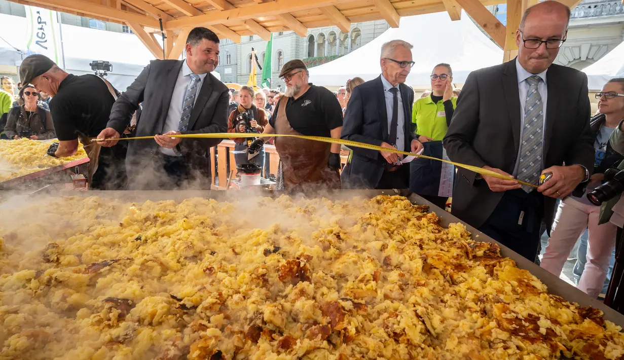 Para pejabat mengukur penggorengan raksasa selama upaya rekor rösti terbesar di dunia sebagai bagian dari acara yang menandai peringatan 125 tahun Serikat Petani Swiss (SBV) di Bern, Swiss pada 19 September 2022. Petani Swiss berhasil memecahkan rekor roesti terbesar di dunia yang dibuat di atas wajan berbentuk salib dengan ukuran 13.7 meter persegi. (Fabrice COFFRINI / AFP)