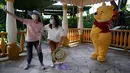 Pengunjung yang mengenakan masker berswafoto dengan karakter kartun Winnie the Pooh di Disneyland Hong Kong pada Jumat (25/9/2020). Setelah dibuka dan tutup kembali, Disneyland Hong Kong dibuka kembali untuk wisatawan. (AP Photo/Kin Cheung)