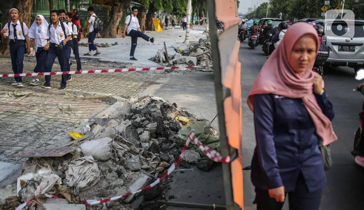 Pelajar melintasi trotoar yang sedang direvitalisasi di kawasan Kramat Raya, Jakarta, Rabu (6/11/2019). Ketua Koalisi Pejalan Kaki Alfred Sitorus menilai pengerjaan revitalisasi trotoar membahayakan pejalan kaki karena tidak ada ruang sementara untuk melintas. (Liputan6.com/Faizal Fanani)