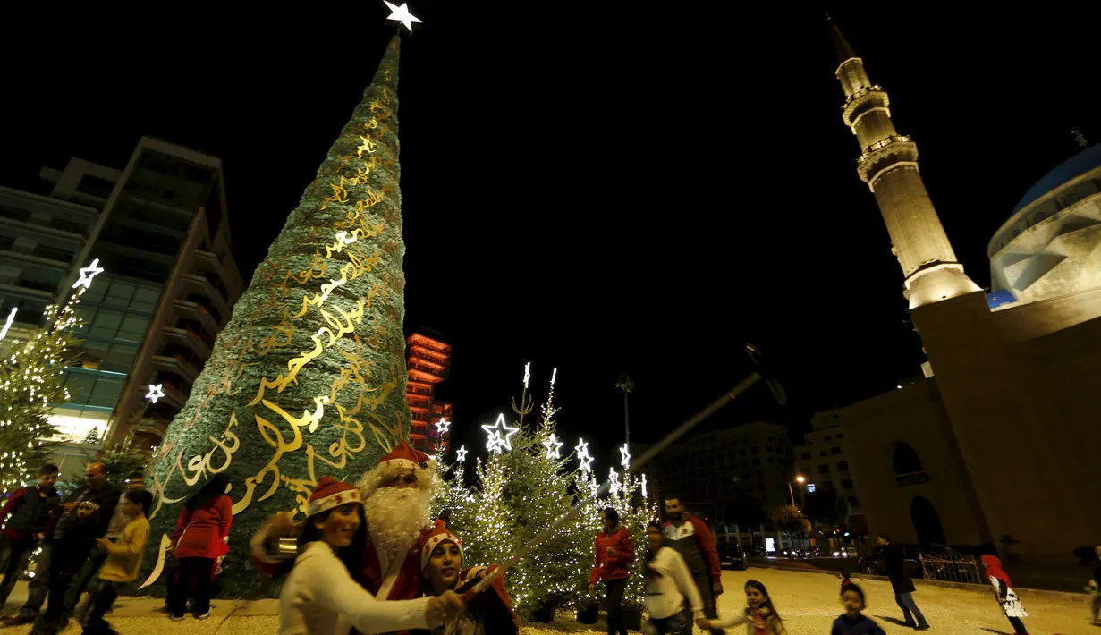 Seorang anak berselfie dengan pria berkostum Sinterklas dengan latar belakang pohon Natal yang dirancang oleh desainer Lebanon, Elie Saab di depan Masjid Al-Amin, di pusat kota Beirut, 12 Desember 2015. (REUTERS/Jamal Saidi)
