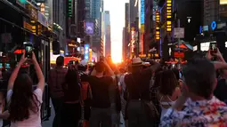 Orang-orang mengambil gambar fenomena Manhattanhenge, dimana matahari terbenam sejajar tepat dengan jalan, di 42nd street di Times Square, New York City, Kamis (12/7). Fenomena ini hanya terjadi selama beberapa hari dalam setahun. (AFP/TIMOTHY A. CLARY)