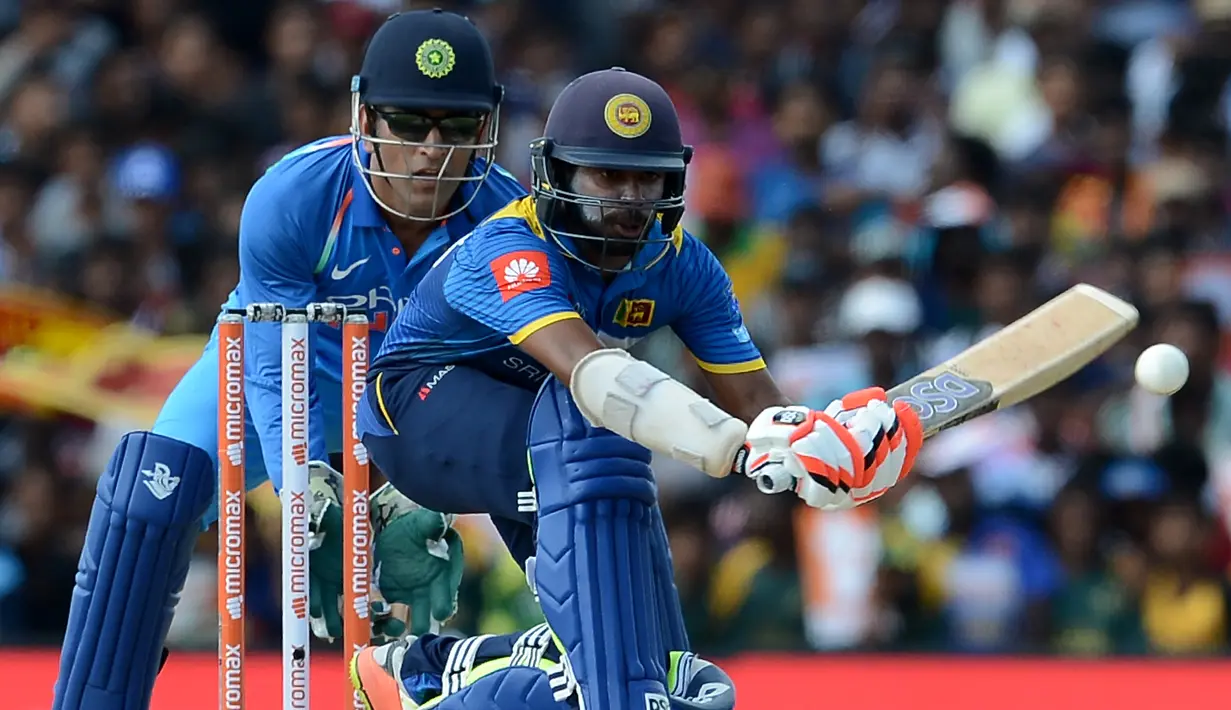 Pemain kriket Sri Lanka Niroshan Dickwella (kana) diawasi oleh wicketkeeper India Mahendra Singh Dhoni burusaha memukul bola dalam pertandingan kriket One Day International (ODI) di Dambulla (20/8). (AFP Photo/Lakruwan Wanniarachchi)