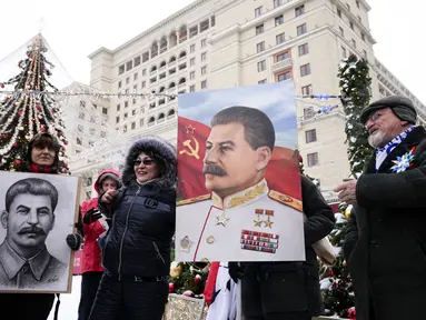 Orang-orang berfoto sambil memegang potret pemimpin Soviet Josef Stalin sebelum meletakkan bunga di makamnya menandai peringatan 142 tahun kelahirannya di dekat Tembok Kremlin di Lapangan Merah di Moskow, Rusia, Selasa (21/12/2021). (AP Photo/Alexander Zemlianichenko)