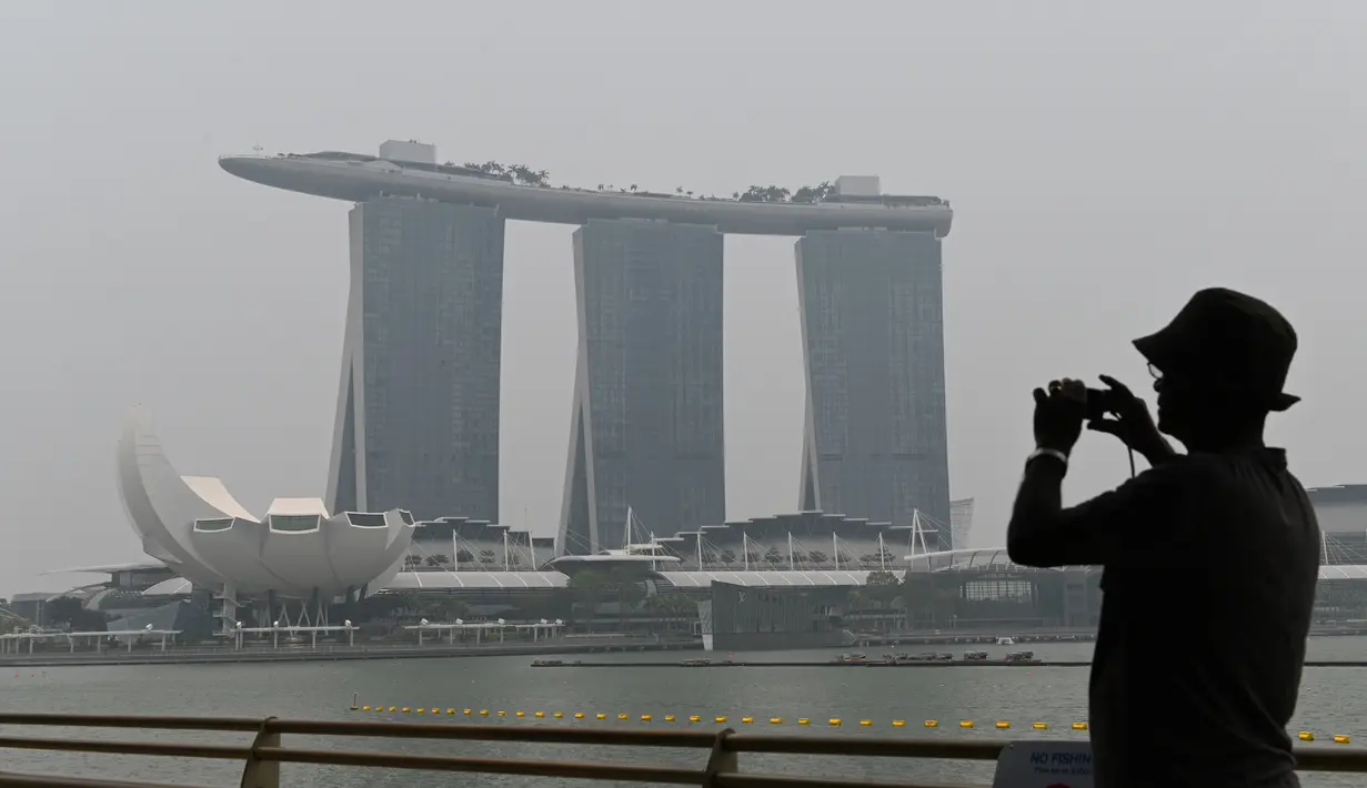 Seorang pria mengambil gambar ketika Hotel dan Resor Marina Bay Sands diselimuti kabut asap, Singapura, Rabu (18/9/2019). Badan Meteorologi Klimatologi dan Geofisika (BMKG) mendeteksi sebaran asap akibat kebakaran hutan dan lahan di Sumatra mencapai Singapura dan Malaysia. (Roslan RAHMAN/AFP)