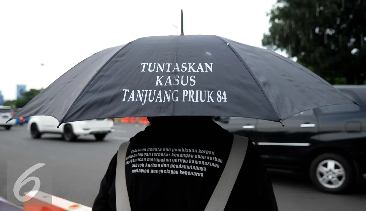 Seorang aktivis Solidaritas Korban untuk Keadilan membawa payung yang bertuliskan seruan aksinya saat menggelar aksi Kamisan di depan Istana Merdeka, Jakarta, Kamis (29/12). (Liputan6.com/Gempur M Surya)
