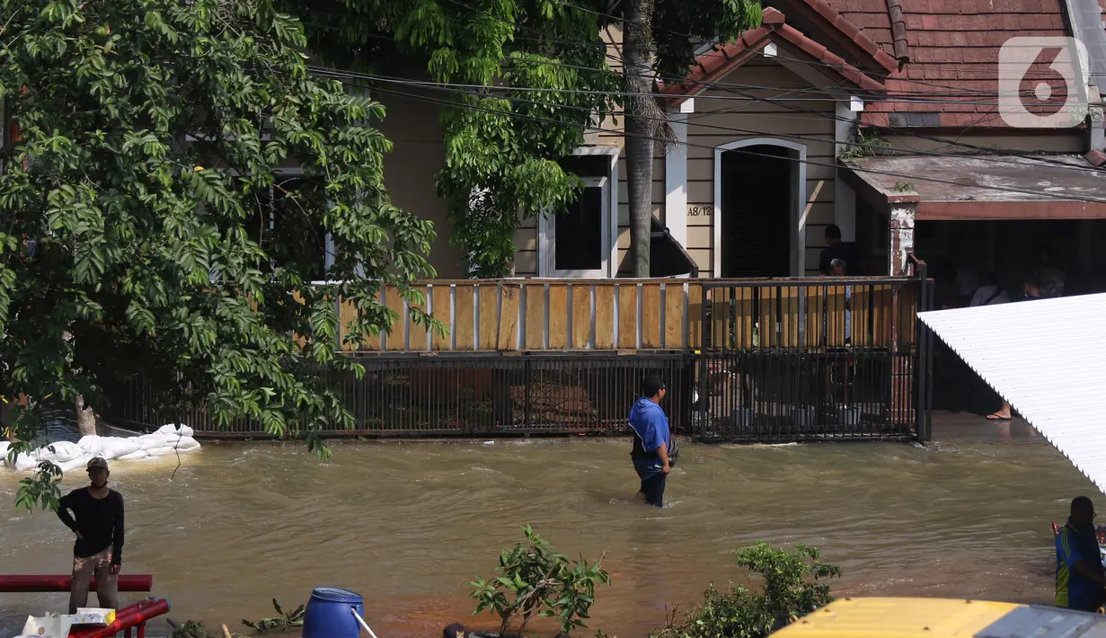 Warga melintasi banjir akibat jebolnya tanggul karena tertimpa tanah longsor, di Perumahan Nerada Estate Ciputat, Tangerang Selatan, Sabtu (12/6/2021). Longsor yang menimpa sejumlah rumah membuat tanggul pembatas kali jebol dan air meluap sehingga menyebabkan banjir. (Liputan6.com/Angga Yuniar)