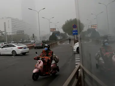 Seorang wanita mengendarai sepeda listrik mengenakan masker di sebuah jalan yang diselimuti kabut asap tebal di Beijing, China (14/11). Pihak berwenang mengeluarkan peringatan kuning untuk polusi udara buruk pada hari Rabu. (AP Photo/Andy Wong)