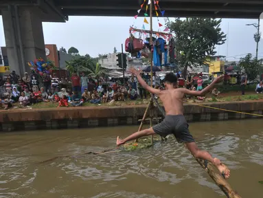 Warga Kalimalang mencoba melewati bambu yang telang dilumuri oli untuk mencapai pinang dalam lomba Titian Bambu di RW 04, Kelurahan Cipinang Melayu, Kecamatan Makasar, Jakarta Timur, Sabtu (24/8/2024). (merdeka.com/Imam Buhori)