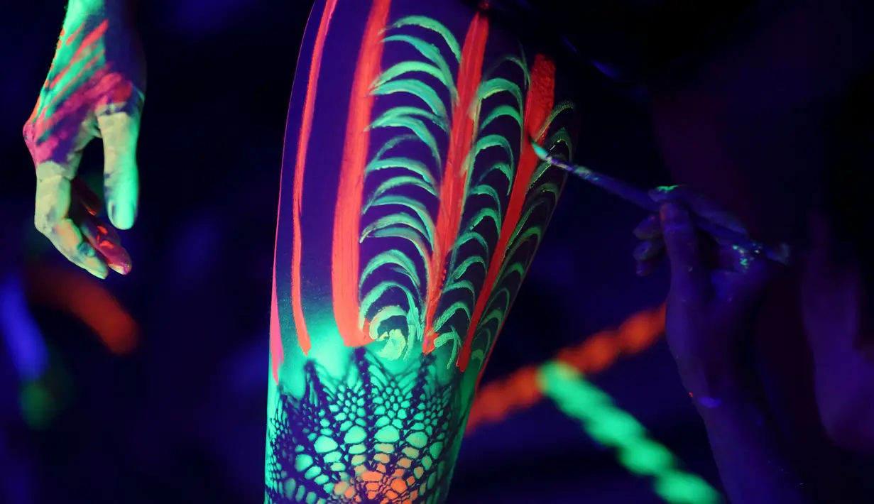 Seorang seniman melukis model di bagian kaki mengunakan cat sinar ultraviolet saat mengikuti Festival Bodypainting Dunia 2015 di Poertschach, Austria, (3/7/2015). Festival ini digelar di Danau Woerthersee, dari tanggal 3-5 Juli. (Reuters/Heinz-Peter Bade)