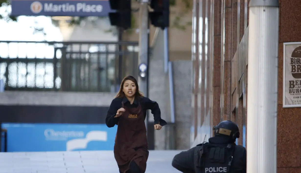 Seorang karyawan yang memakai celemek berlari keluar dari Kafe Lindt, Martin Place, Sydney, Senin (15/12/2014). (REUTERS/Jason Reed)