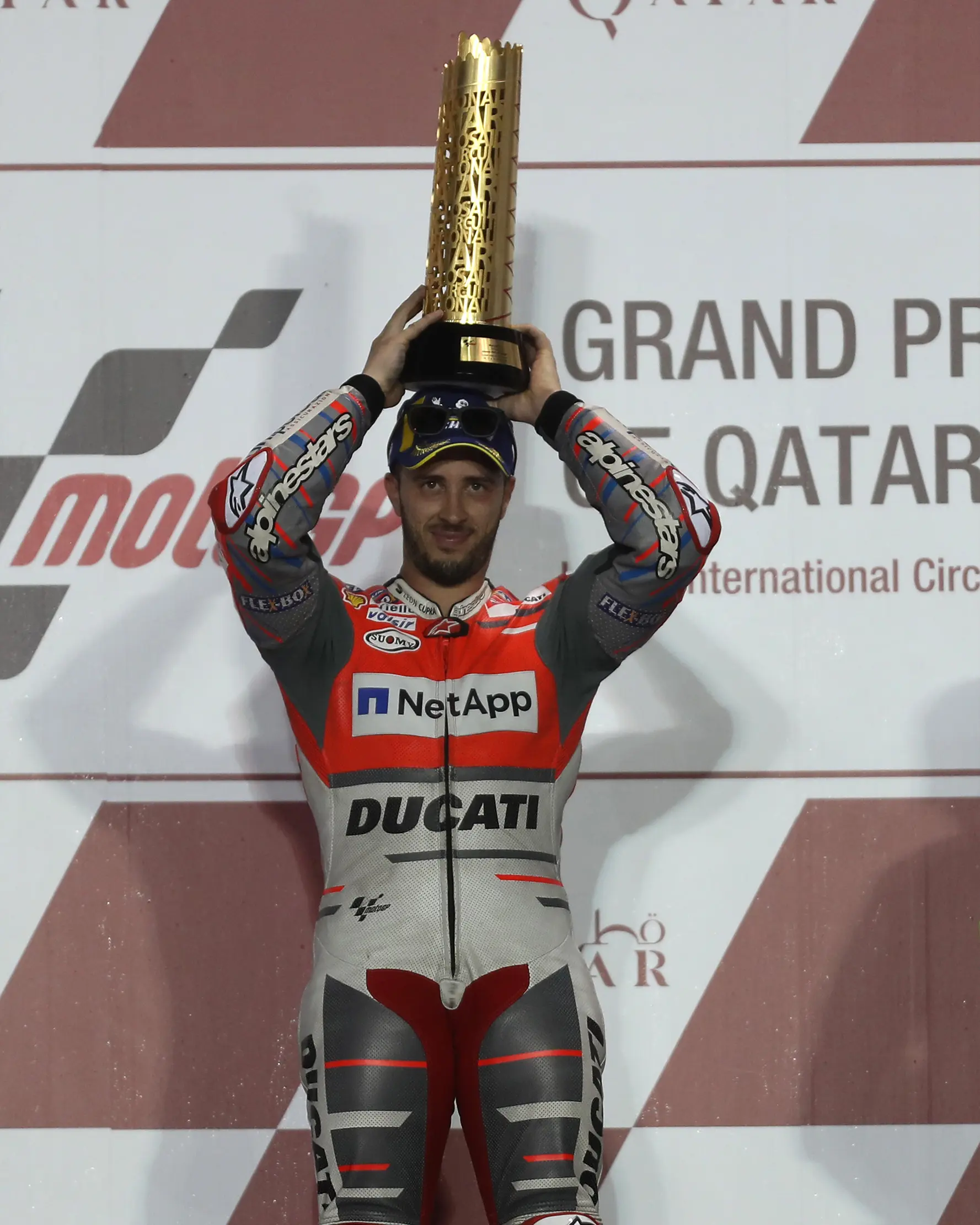 Pembalap Ducati Andrea Dovizioso berpose diatas podium sambil memegang pialanya usai memenangkan balapan di MotoGP Qatar 2018 di Sirkuit Internasional Losail (18/3). (AFP Photo/Karim Jaafar)