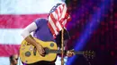 Vokalis grup band Coldplay, Chris Martin menutupi wajahnya dengan bendera Amerika Serikat sambil memainkan gitarnya saat menghibur para penonton di Lapangan FedEx di Landover, Md, AS (6/8). (Photo by Brent N. Clarke/Invision/AP)