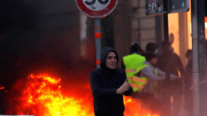 Demonstran berjalan dekat api saat kerusuhan menentang kenaikan harga bahan bakar di Paris, Prancis, Sabtu (24/11). Demonstran tersulut oleh hasutan beberapa oknum sehingga memicu kerusuhan. (AP Photo/Christophe Ena)