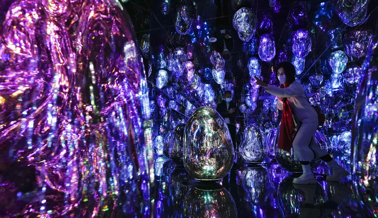 Seorang wanita bertopeng memberi isyarat saat pengunjung berinteraksi dengan instalasi seni digital imersif berjudul “Resonating Microcosms, Solidified Light Color” di museum "teamLab Massless" yang baru dibuka di Beijing, China, Senin (26/12/2022). Berbasis di Tokyo teamLab membuat museum seni digital yang memamerkan berbagai karya seni interaktif di dalam pusat perbelanjaan di ibu kota Beijing. (AP Photo/Andy Wong)