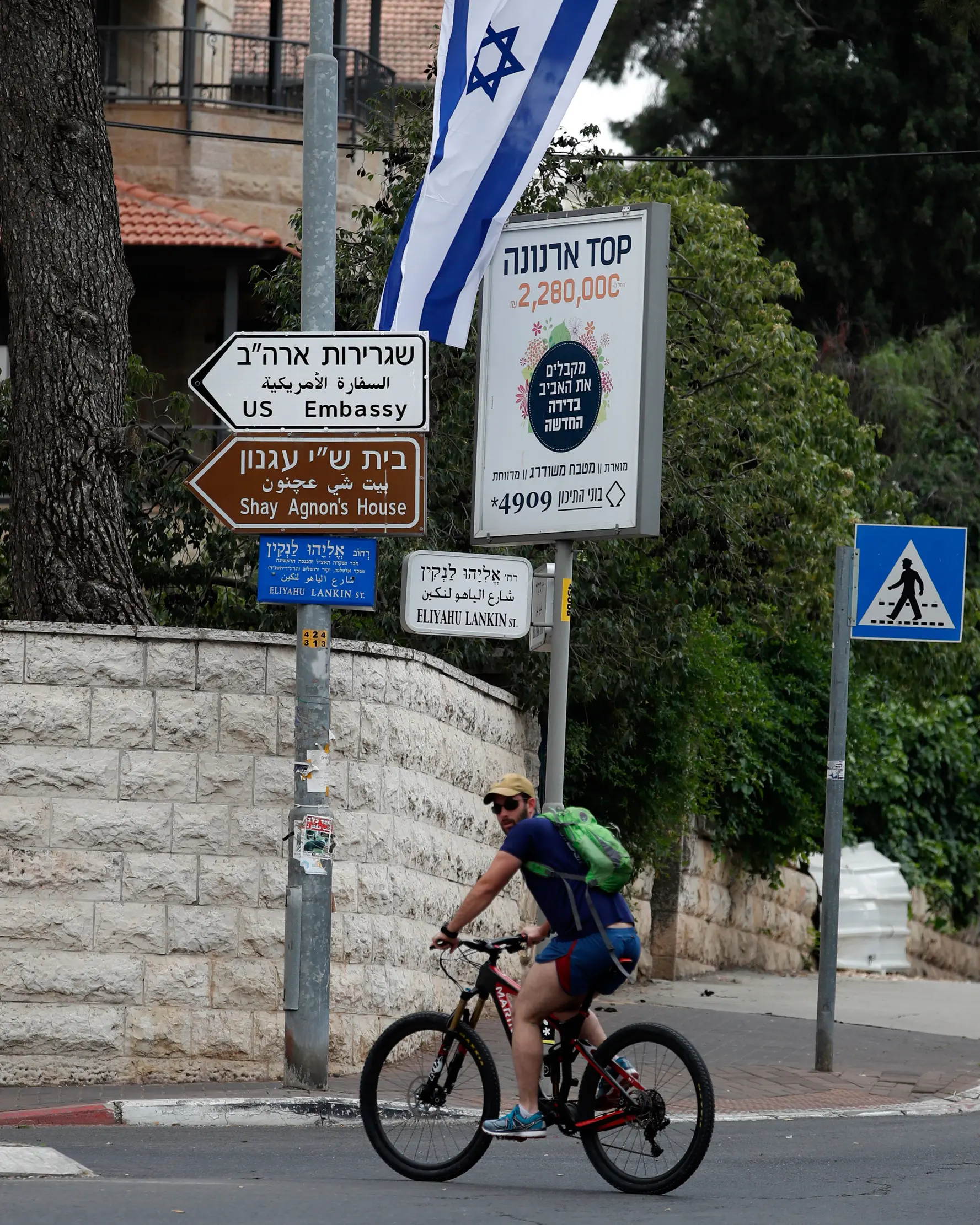 Pesepeda melintas dekat tanda jalan yang menunjukan arah Kedutaan Besar Amerika Serikat (AS) di Yerusalem, Senin (7/5). Rencananya, AS akan memindahkan Kedubes mereka ke Yerusalem pada 14 Mei mendatang. (AFP/THOMAS COEX)