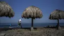 Seorang turis, mengenakan masker, berjalan di sepanjang pantai di Havana, Kuba, pada 2 Maret 2021. Kepulauan Karibia memburu pengunjung untuk menggerakkan kembali roda ekonomi yang terhenti di salah satu kawasan di dunia yang sangat bergantung dengan sektor pariwisata. (AP Photo/Ramon Espinosa)