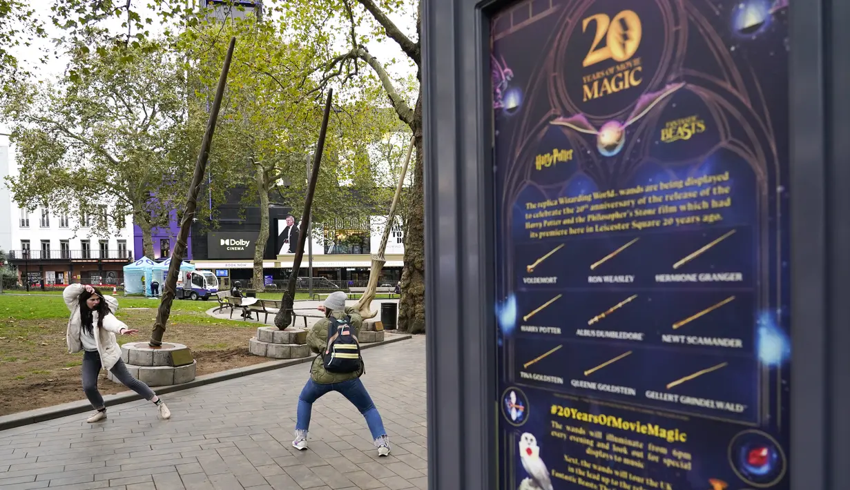Orang-orang berpose di bawah tongkat raksasa untuk peringatan 20 tahun film Harry Potter and the Philosopher's Stone di Leicester Square, London, Rabu (13/10/2021). Instalasi terdiri dari sembilan tongkat setinggi 15 kaki yang mewakili sembilan karakter kunci dari film. (AP Photo/Alberto Pezzali)