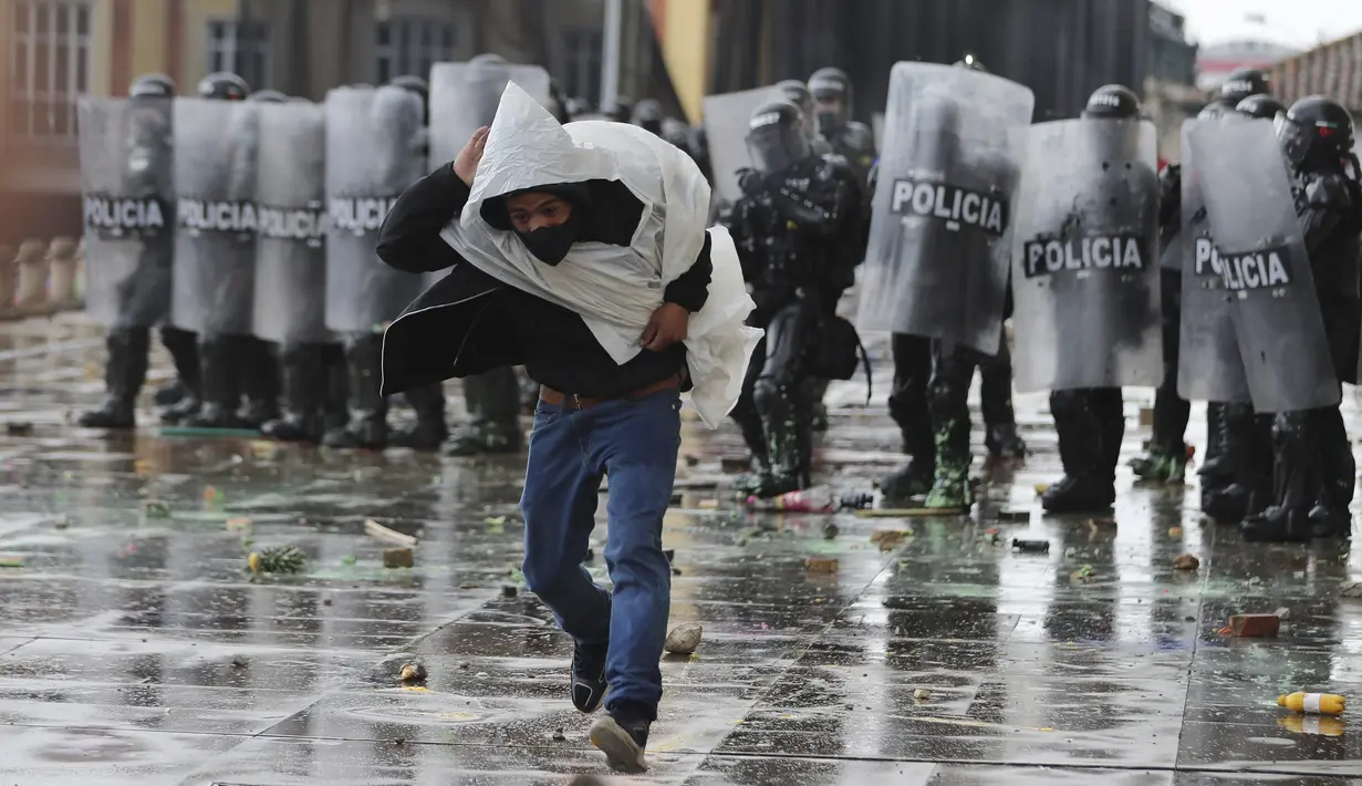 Seorang pria melarikan diri dari polisi setelah melemparkan batu ke arah mereka selama pemogokan nasional untuk memprotes reformasi pajak yang diusulkan pemerintah, di Bogota, Kolombia, Rabu (28/4/2021). (AP Photo/Fernando Vergara)