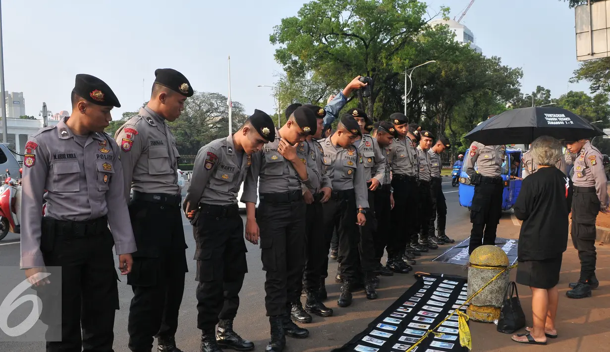 Aparat kepolisian melihat foto-foto yang pajang saat aksi kamisan di depan Istana Negara, Jakarta, Kamis (2/7/15). Dalam aksinya mereka meminta kepada Jokowi untuk menuntaskan kasus pembunuhan Jopi. (Liputan6.com/Herman Zakharia)
