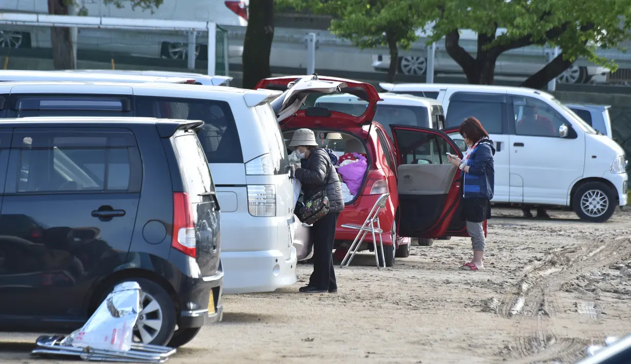 Dua orang wanita berdiri di dekat mobil mereka di Mashiki, prefektur Kumamoto, Jepang, 17 April 2016. Gempa yang terjadi pada Kamis (14/4) malam membuat banyak warga lebih memilih untuk mengungsi dan tidur di mobil mereka sendiri. (Kazuhiro NOGI/AFP)
