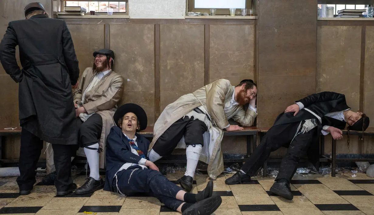 Pria Yahudi ultraortodoks beristirahat setelah mabuk saat perayaan Hari Raya Purim di lingkungan ultraortodoks Mea Shearim, Yerusalem, 8 Maret 2023. Hari Raya Purim merupakan perayaan keselamatan orang Yahudi dari genosida di Persia kuno, seperti yang diceritakan dalam Gulungan Ester. (AP Photo/Ohad Zwigenberg)