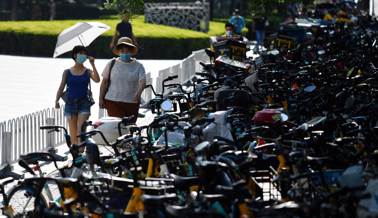 Dua orang wanita berjalan melintasi sepeda-sepeda yang diparkir memenuhi trotoar di Beijing, China (21/7/2020).  Seperti diketahui Beijing telah menerapkan bike sharing yang sudah tersedia di trotoar-trotoar Kota Beijing. (AFP Photo/Greg Baker)