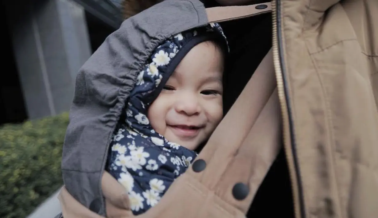 Senyum dari bibir mungilnya dengan mata yang sipit, Natusha mengumpat dibalik kain gendongan sang ibu. Ia tampak begitu nyaman saat berada di dekapan wanita yang telah melahirkannya. (Instagram/natushaa.oliviaa.alinskie)