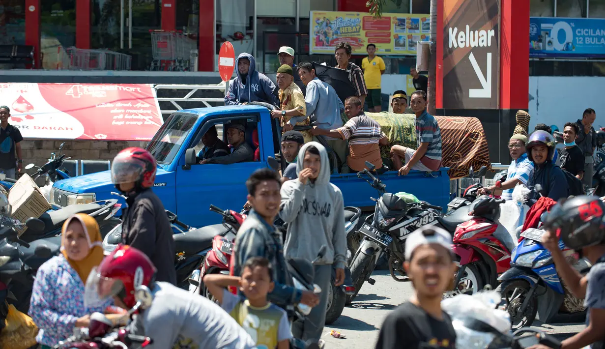 Sebuah mobil yang membawa peti mati dari kerabat mereka melintas saat warga menjarah toko serba ada setelah gempa dan tsunami di Palu, Sulteng, Minggu (30/9). Warga terpaksa mengambil karena membutuhkan makanan dan air bersih. (AFP PHOTO/BAY ISMOYO)
