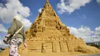 Seorang wanita berjalan melewati patung pasir tertinggi di dunia, yang sedang dibangun di Blokhus, Denmark, Rabu (7//2021). Memiliki ketinggian 21,16 meter, istana ini mengalahkan rekor dunia istana pasir tertinggi sebelumnya yang dipegang Jerman pada 2019. (Claus Bjoern Larsen/Ritzau Scanpix/AFP)