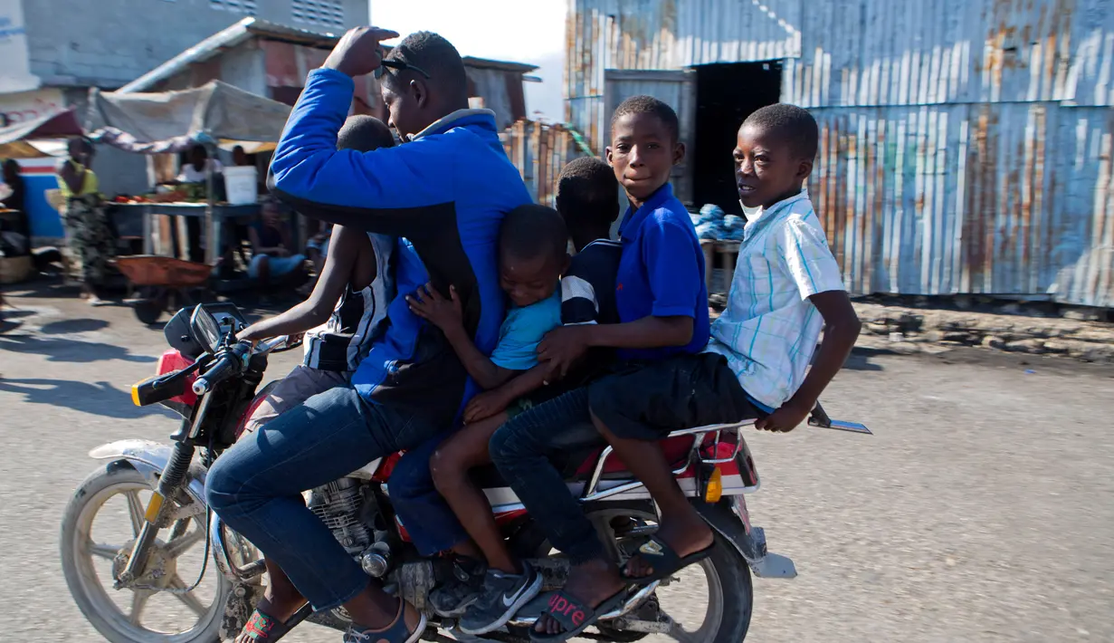 Pengendara motor membawa lima penumpang melewati area Cite Soleil di Port-au-Prince, Haiti (17/3). Daerah ini umumnya dianggap sebagai salah satu daerah termiskin dan paling berbahaya di Belahan Barat. (AP Photo/Dieu Nalio Chery)