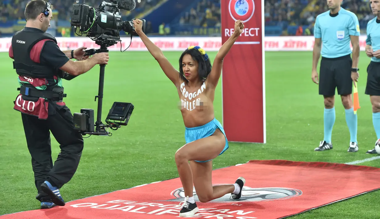 Seorang wanita bertelanjang dada berpose didalam lapangan sebelum pertandingan kualifikasi Piala Dunia 2018 antara Ukraina dan Turki di Kharkiv (2/9). Wanita itu memprotes rezim Erdogan yang dinilai telah membunuh kebebasan. (AFP Photo/Sergei Supinsky)