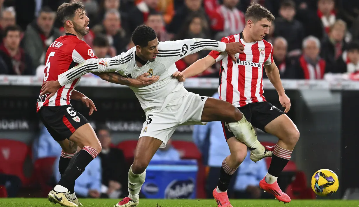 <p>Pemain Real Madrid, Jude Bellingham, berebut bola dengan pemain Athletic Bilbao, Mikel Jauregizar (kanan) dan Yeray Alvarez (kiri), pada laga lanjutan Liga Spanyol 2024/2025 di San Mames Stadium, Bilbao, Spanyol, Kamis (05/12/2024) dini hari WIB. (AP Photo/Miguel Oses)</p>