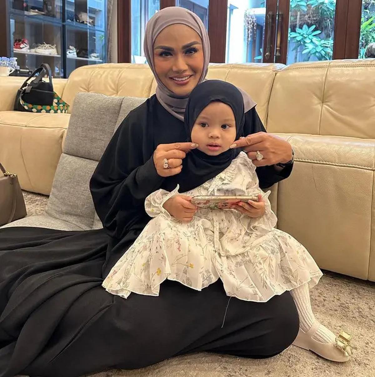 Krisdayanti memangku Ameena yang menggemaskan, dengan dress putih dan hijab hitam.