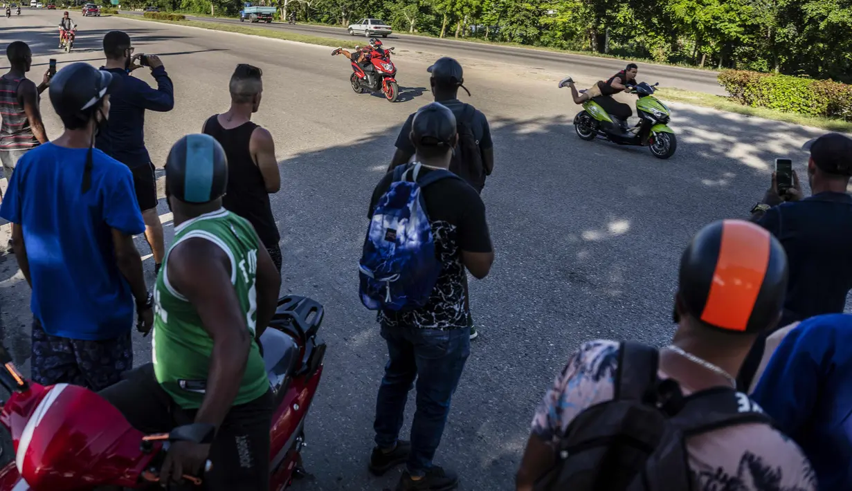 Orang-orang menonton drag race antara dua pengendara skuter listrik pada pertemuan sore untuk memamerkan aksi dan balapan di Havana, Kuba, pada 15 Juli 2022. Kuba telah dibanjiri dalam beberapa tahun terakhir dengan "motorinas", begitu skuter listrik ini disebut di pulau itu, sebuah mode bagi banyak orang, tetapi juga solusi untuk masalah transportasi dan kekurangan bahan bakar yang melanda negara Karibia itu. (AP Photo/Ramon Espinosa)