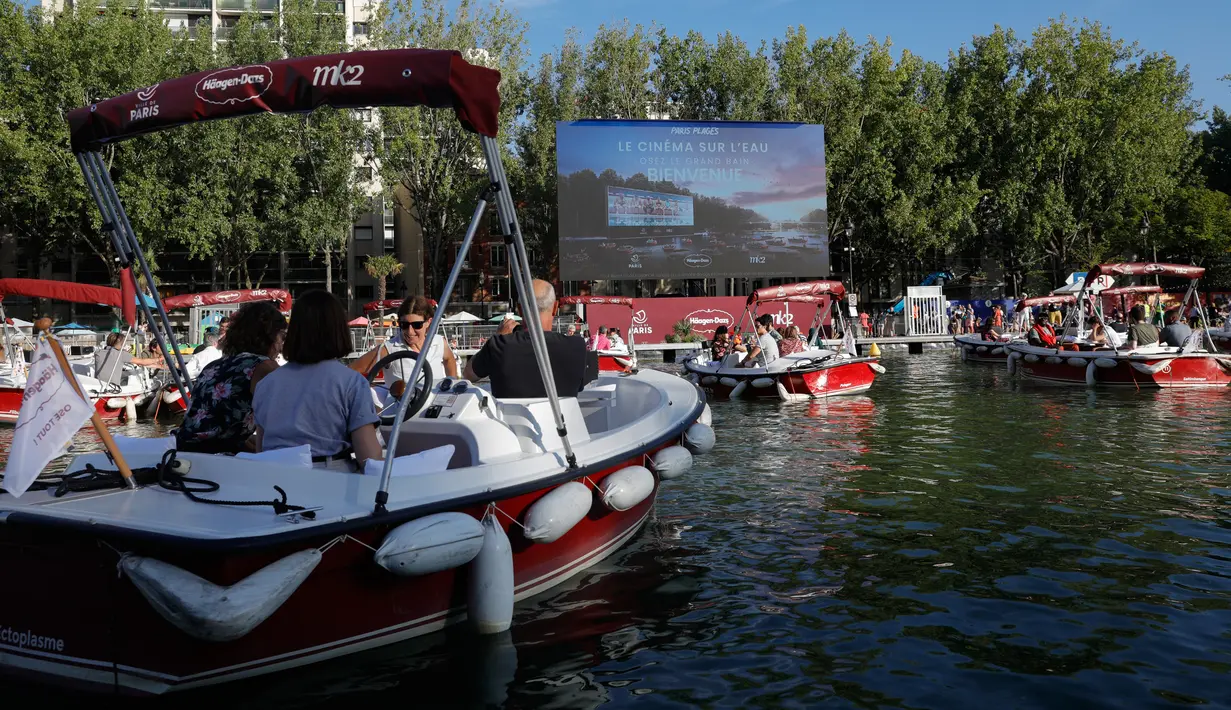 Orang-orang menghadiri pemutaran film "Le grand bain" pada hari pertama acara musim panas "Paris-Plages" di La villette bassin, Paris, 18 Juli 2020. Paris menghadirkan sebuah terobosan baru dengan bioskop terapung lengkap dengan perahu yang tetap menjaga jarak sosial. (GEOFFROY VAN DER HASSELT/AFP)
