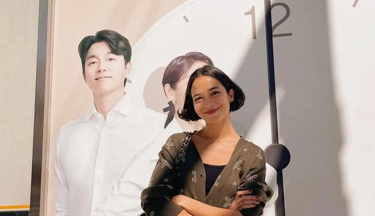 Berpose dengan poster idolanya, Gong Yoo, Putri Marino tampil chic dengan cardigan, tank top, dan high waisted jeans. Shoulder bag hitam pun melengkapi penampilannya.  (Instagram/putrimarino)