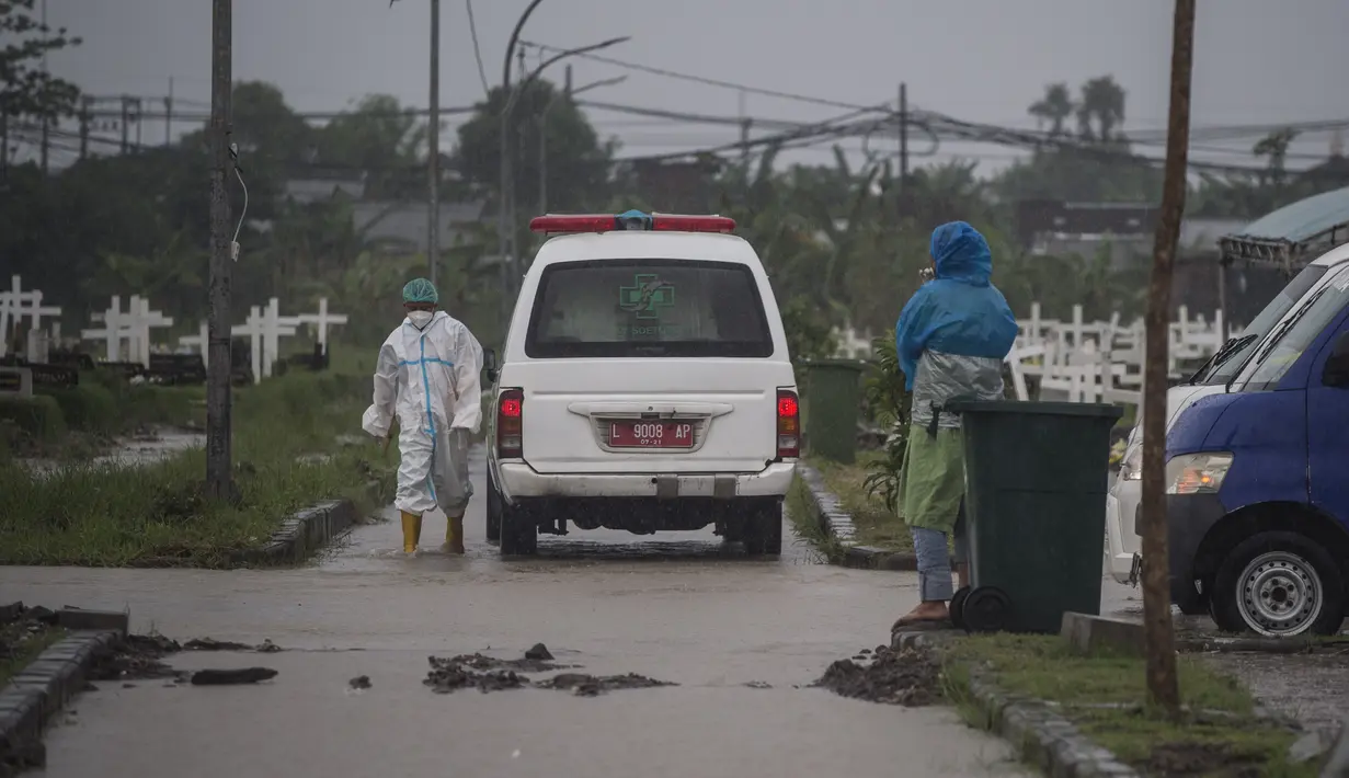 Sebuah mobil van membawa jenazah korban virus Corona Covid-19 untuk dimakamkan di tengah hujan lebat di pemakaman Keputih, Surabaya (7/1/2020). Pemerintah Kota Surabaya menyediakan tempat di TPU Keputih dan TPU Babat Jerawat untuk lahan pemakaman korban Covid-19. (AFP/Juni Kriswanto)