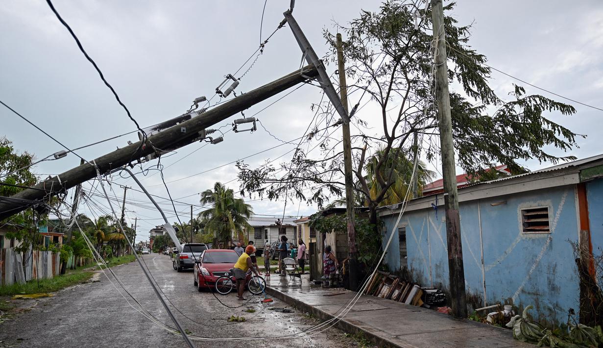 Orang-orang berdiri di jalan dengan tiang listrik tumbang setelah Badai Lisa di Belize City, Belize, 3 November 2022. Badai Tropis Lisa menyebabkan banjir dan membuat sebagian negara itu menjadi gelap gulita. (Johan ORDONEZ/AFP)