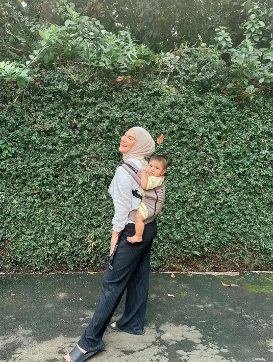 <p>Di foto terbaru yang diunggahnya, Irish Bella tampak menggendong anak keduanya di punggungnya. Ia mengenakan atasan berwarna putih, dipadu dengan celana panjang hitam bergaris, dan hijab cokelat muda. Sang buah hati tampak gemas dengan outfit berwarna kuning. Foto: Instagram.</p>